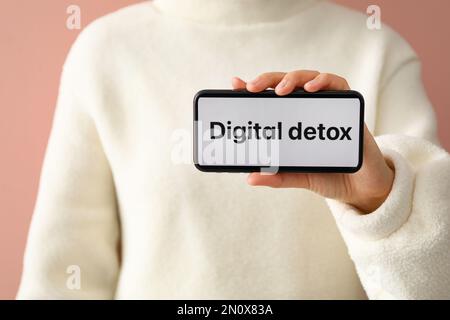 Femme tenant un smartphone avec phrase NUMÉRIQUE DETOX sur l'écran contre fond rose, gros plan Banque D'Images