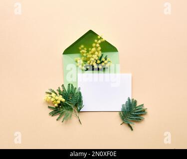 Carte vierge, fleurs mimosa dans une enveloppe verte sur fond jaune doré. Décoration printanière naturelle. Flat lay, vue de dessus, composition centrale. Banque D'Images