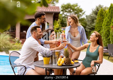 Groupe de jeunes heureux qui applaudissent au cidre près de la piscine dans le jardin Banque D'Images