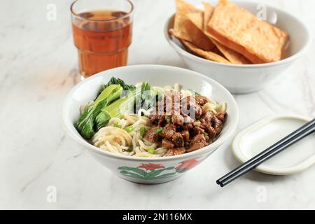 Mie Ayam ou Chicken Noodle, cuisine populaire indonésienne de rue avec Noodle, poulet et légumes verts avec bouillon. Sur la table blanche Banque D'Images