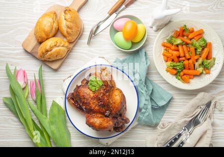 Nourriture de Pâques sur table rustique blanche : œufs pastel, poulet et légumes rôtis, petits pains et fleurs de printemps tulipes vue de dessus plat, famil de Pâques Banque D'Images