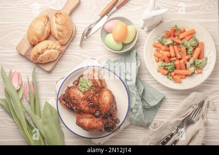 Nourriture de Pâques sur table rustique blanche : œufs pastel, poulet et légumes rôtis, petits pains et fleurs de printemps tulipes vue de dessus plat, famil de Pâques Banque D'Images