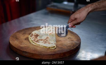 Couper une tortilla pliée avec un couteau à rôtis par le chef dans un restaurant. Banque D'Images