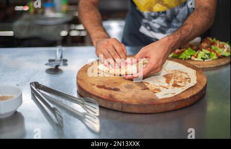 Un chef prépare une assiette de falafel et des tortillas sur une planche à découper ronde en bois dans la cuisine. Banque D'Images