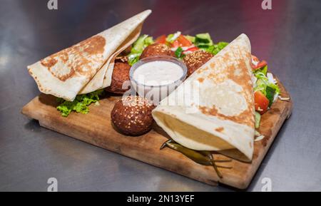 Présentation du plat libanais du Moyen-Orient Falafel sur une assiette en bois. tortilla, salade de légumes et sauce tahini. Banque D'Images