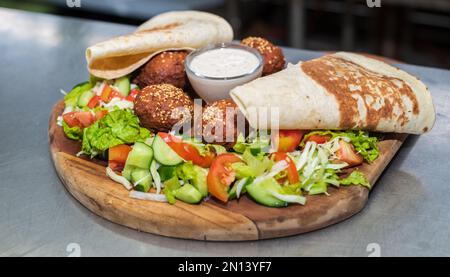 Un délicieux plat de départ, le Falafel, sur une assiette en bois dans la cuisine du restaurant libanais. pain plat, salade de légumes et sauce tahini. Banque D'Images