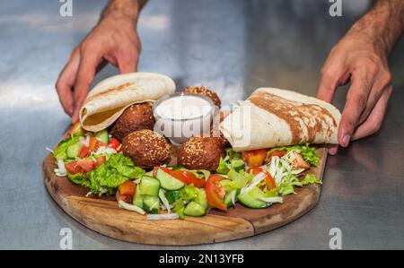 Présentation du plat libanais du Moyen-Orient Falafel sur une assiette en bois. tortilla, salade de légumes et sauce tahini. Banque D'Images