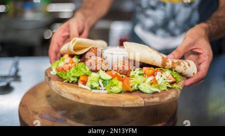 Présentation du plat libanais du Moyen-Orient Falafel sur une assiette en bois. tortilla, salade de légumes et sauce tahini. Banque D'Images