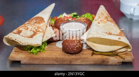 Présentation du plat libanais du Moyen-Orient Falafel sur une assiette en bois. tortilla, salade de légumes et sauce tahini. Banque D'Images