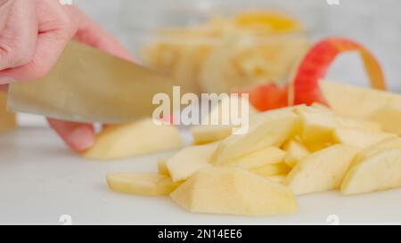 Les tranches de pomme et le zeste de pomme sur une planche à découper blanche sur la table de cuisine. Femme en tranches de pommes, recette de gâteau de pomme Banque D'Images