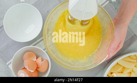 Mélanger les oeufs et le sucre dans un bol en verre, plat, les mains de femme. Recette de gâteau aux pommes Banque D'Images