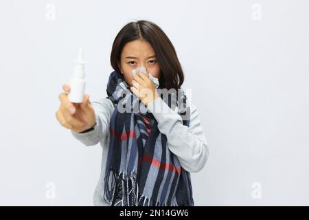 Asiatique femme grippe rhume avec le nez étouffant tient allergie spray nasal avec mal de gorge sur fond blanc Banque D'Images