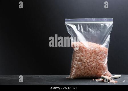Sel himalayan rose dans un sac en plastique sur la table, sur fond sombre, espace pour le texte Banque D'Images