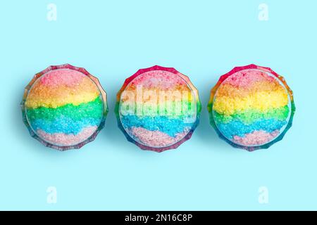 Glace à raser arc-en-ciel dans des bols à dessert en verre sur fond bleu clair, plat Banque D'Images