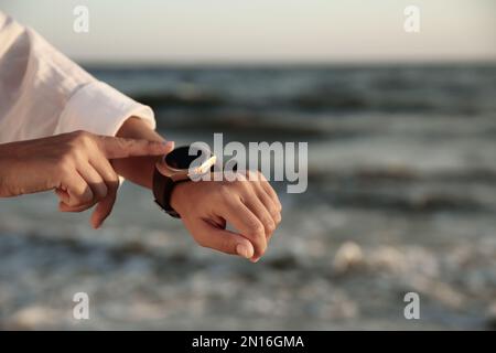 Jeune femme regardant une montre intelligente sur la plage au coucher du soleil, en gros plan Banque D'Images