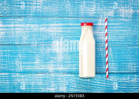 Bouteille de lait et paille en papier sur fond en bois bleu, plat. Banque D'Images