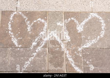 Gros plan de coeurs dessinant avec de la craie blanche sur la texture de la chaussée en béton gris comme symbole d'amour concept urbain extérieur Banque D'Images