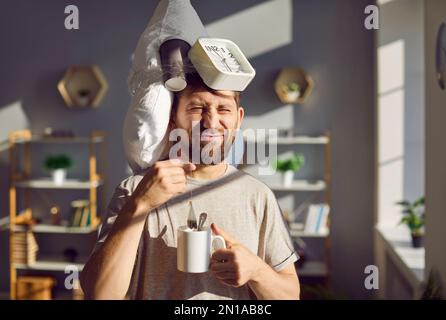 Un homme endormi assis sur son lit se réveillant en train de préparer du thé dans une tasse à la maison. Banque D'Images