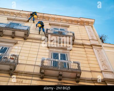 TARANTO, ITALIE - 29 OCTOBRE 2021 : deux ouvriers nettoyant la façade de la maison historique accrochée à des cordes Banque D'Images