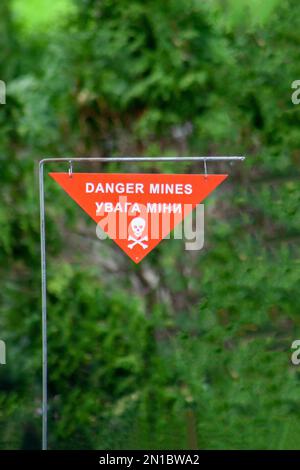 Mines de danger. Symbole d'avertissement de champ de mines Sapper sur fond vert. Jolly Roger - crossos blancs du crâne sur un signe rouge du danger des mines terrestres. Mine militaire. La guerre en Ukraine. Traduction ukrainienne Banque D'Images