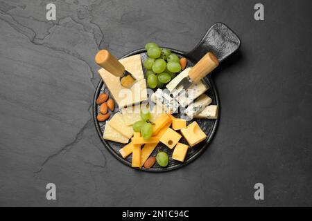 Plateau de fromages avec couteau spécialisé et fourchette sur table noire, vue de dessus Banque D'Images