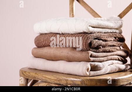 Pile de chandails chauds pliés sur une chaise en bois sur fond clair Banque D'Images