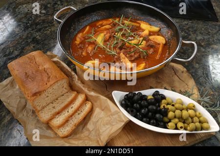 Bœuf braisé dans une sauce au vin rouge servi avec des pommes de terre cuites au four, du pain, des olives et du romarin. Banque D'Images