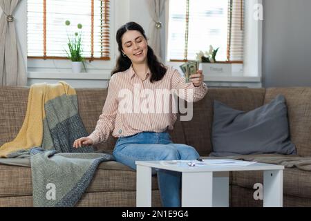 Achat de biens immobiliers. Une jeune femme de race blanche heureuse assise sur un canapé met de l'argent sur une table. Concept de crédit-bail, d'affaires et d'hypothèque. Banque D'Images