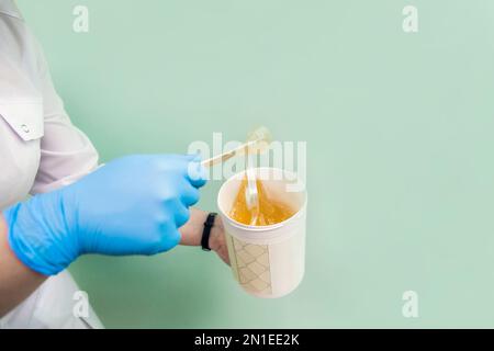 Le cosmétologue tient un pot de cire de sucre, montre la texture de la pâte avec une spatule. Banque D'Images