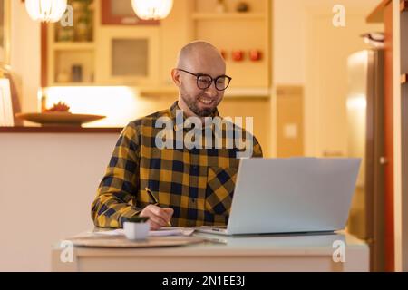Portrait d'un jeune homme du Caucase portant des lunettes souriant et travaillant sur un ordinateur portable. Travailleur utilisant un ordinateur. Concept de travail à distance et freelance. Banque D'Images