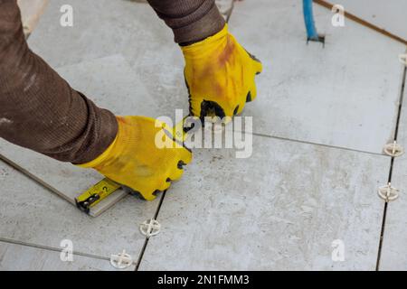 Pendant que l'entrepreneur se prépare à poser des carreaux de céramique sur le sol, il mesure les carreaux avant des couper Banque D'Images