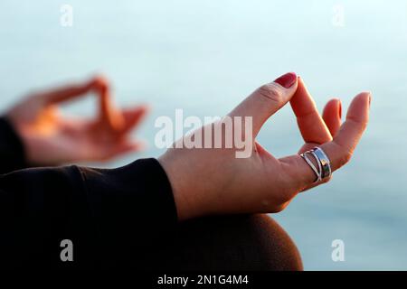 Femme pratiquant la méditation de yoga par la mer au coucher du soleil comme concept de silence et de détente, gros plan sur la main, gyan mudra, Espagne, Europe Banque D'Images