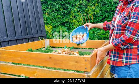 Bac à compost en bois fait à la main. Une femme dans une chemise à carreaux jette les déchets alimentaires dans un bac à compost de bricolage. Préparation de compost à partir de déchets organiques pour Banque D'Images