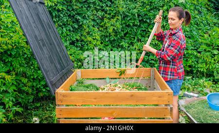 Faire du compost à partir de déchets organiques dans le jardin. Une femme agite les déchets dans un bac à compost en bois avec une fourche. Utilisation des déchets de cuisine pour faire du compost. Po Banque D'Images