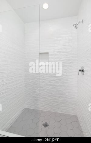 Douche à l'italienne avec carrelage de métro ondulé blanc, carrelage hexagonal gris et pomme de douche chromée. Banque D'Images