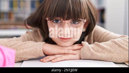 Adorable étudiante hispanique de fille assise sur une table penchée sur le livre en classe Banque D'Images
