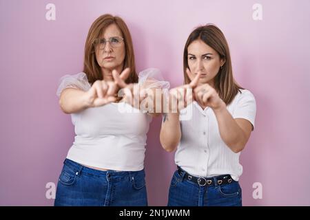 Mère hispanique et fille portant un t-shirt blanc décontracté sur fond rose rejet expression croisant les doigts faisant signe négatif Banque D'Images