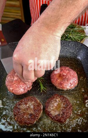 Le chef friture des côtelettes de viande de bœuf pour hamburger dans une poêle à frire avec de l'huile. Faire cuire la préparation du plat de viande dans la cuisine domestique à la maison. Verticale. Gros plan. Banque D'Images