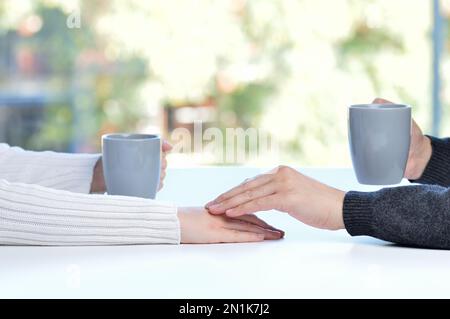 Gros plan d'un homme touchant la main de son partenaire pendant une date dans une table d'un café ou à la maison Banque D'Images