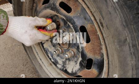 une main dans un gant en tissu enfile un écrou sur un goujon tout en fixant un disque sur une roue de voiture dans le processus de remplacement du caoutchouc en automne ou au printemps saison Banque D'Images