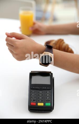 Femme utilisant la montre intelligente pour le paiement sans contact via le terminal dans le café, à proximité Banque D'Images