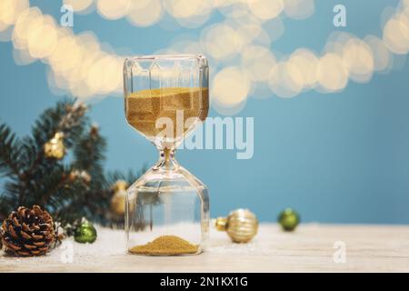 HourGlass, brindilles de sapin et décor sur table blanche contre des lumières floues, espace pour le texte. Compte à rebours de Noël Banque D'Images