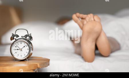 Jambes de la jeune femme européenne se trouve et dort sur blanc lit confortable, foyer sélectif sur le réveil sur table Banque D'Images