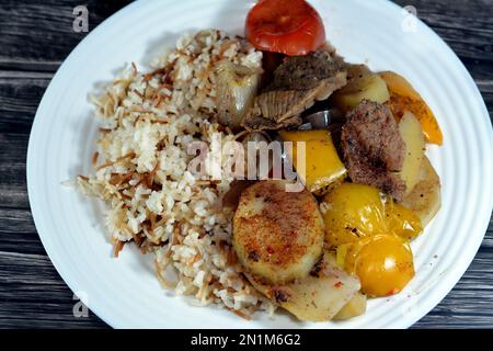 Une assiette de riz égyptien avec vermicelles cuites à la vapeur chaude avec des tranches de pommes de terre cuites au four, oignon, tomate, poivre coloré, morceaux de viande, épices, guar Banque D'Images