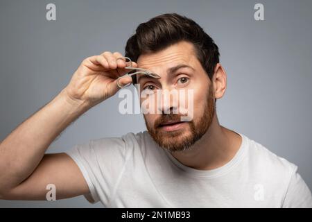 Soin du visage et du bien-être pour hommes. Beau homme barbu d'âge moyen, bruitant les sourcils, fond gris Banque D'Images