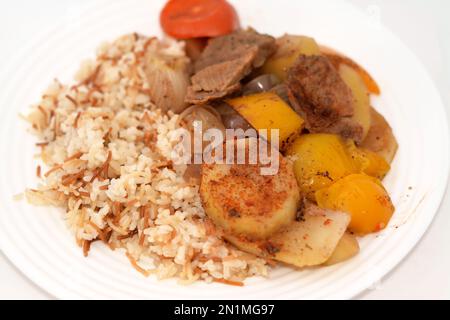 Une assiette de riz égyptien avec vermicelles cuites à la vapeur chaude avec des tranches de pommes de terre cuites au four, oignon, tomate, poivre coloré, morceaux de viande, épices, guar Banque D'Images