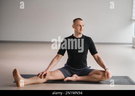 Un homme de construction athlétique fait du yoga dans la salle de gym sur un tapis. Banque D'Images