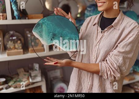 Femme décorateur montre un plateau en verre de résine époxy fait main avec des vagues de mer debout dans son propre studio Banque D'Images