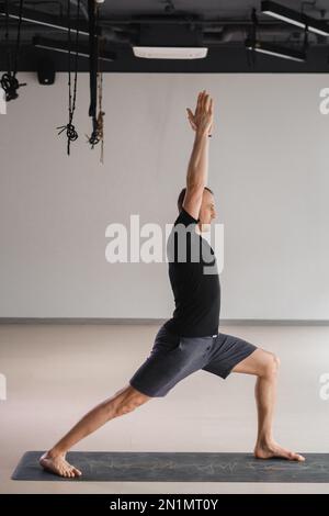 Un homme de construction athlétique fait du yoga dans la salle de gym sur un tapis. Banque D'Images