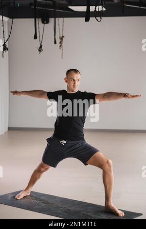 Un homme de construction athlétique fait du yoga dans la salle de gym sur un tapis. Banque D'Images